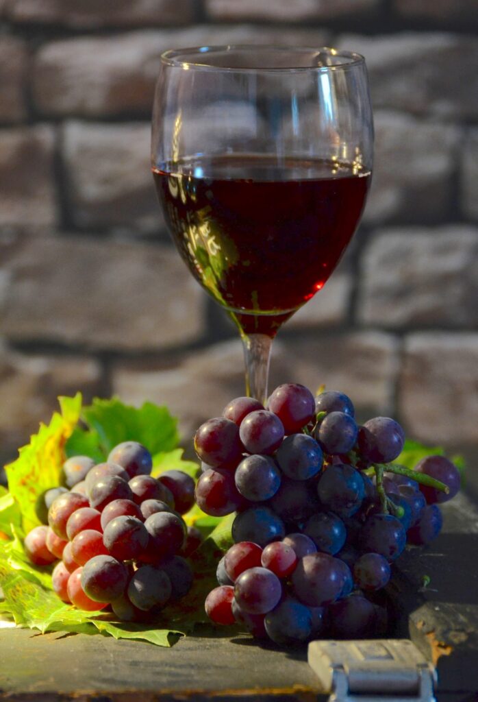 A glass of red wine and s bunch of grapes with leaves on table, brick background