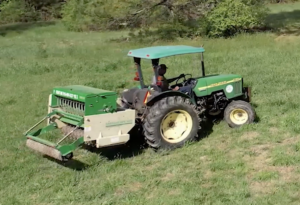 farmer towing seed drill behind a tractor.