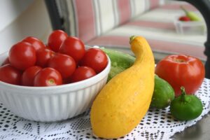 tomatoes in bowl, a squash, pepper, tomato and acucumber on table