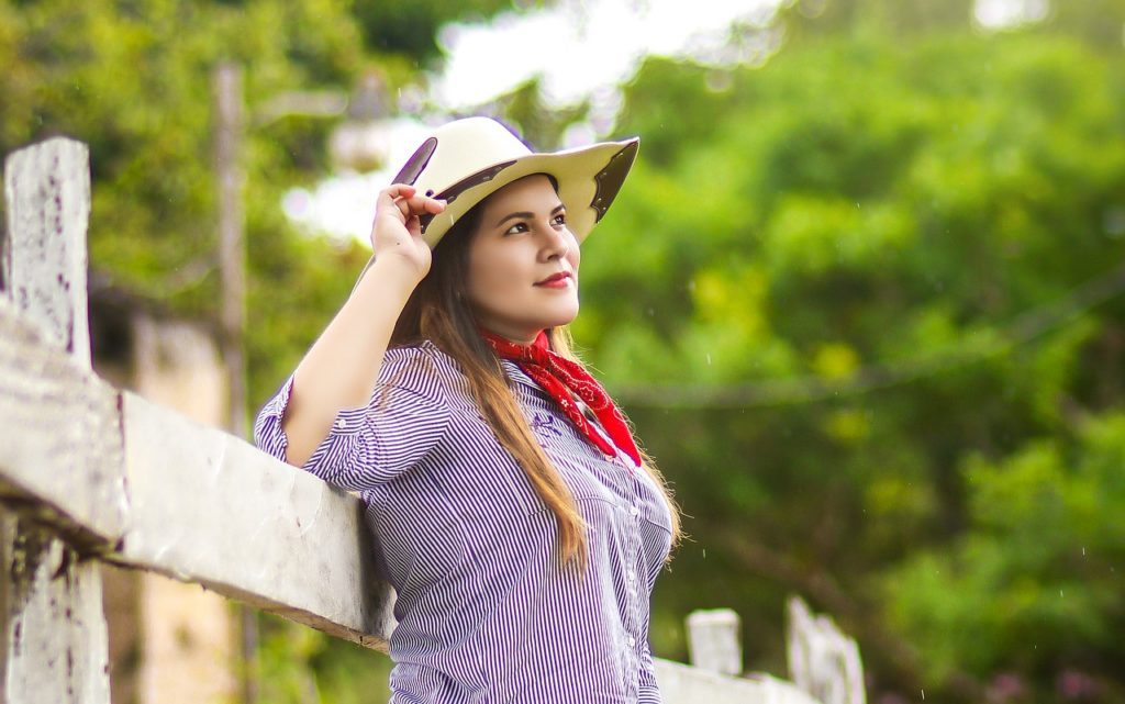 woman wearing a cowboy hat leaning on a fence